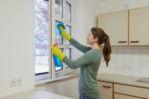 Junge Hauswirtschafterin reinigt Fenster in einer Küche