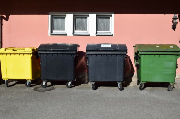 Ein gelber, zwei schwarze sowie ein grüner Müllcontainer vor einem hauswirtschaftlichem Betrieb