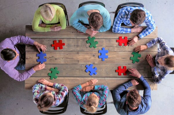 Gruppenbild einer Gruppe von oben, die Puzzlestücke auf einem Tisch zusammenfügt.
