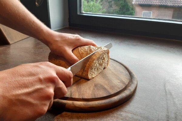 Person schneidet Brot auf einem Holzbrett.