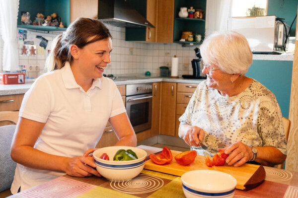 Hauswirtschafterin bereitet gemeinsam mit Seniorin Essen in der Küche vor.