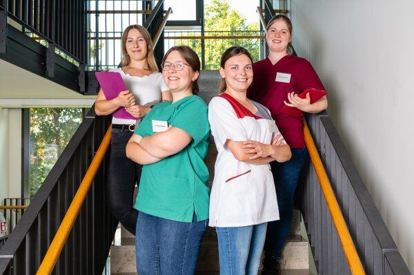 Vier Hauswirtschafterinnen in unterschiedlicher Arbeitskleidung auf einer Treppe.