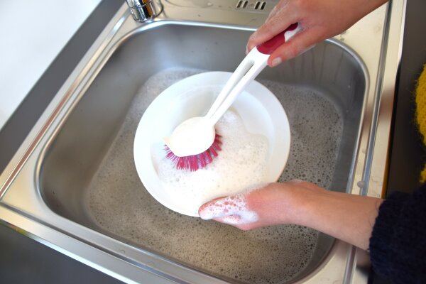 Eine Person Spült Geschirr in einem Geschirrspülbecken aus Edelstahl und verwendet eine Spülbürste.