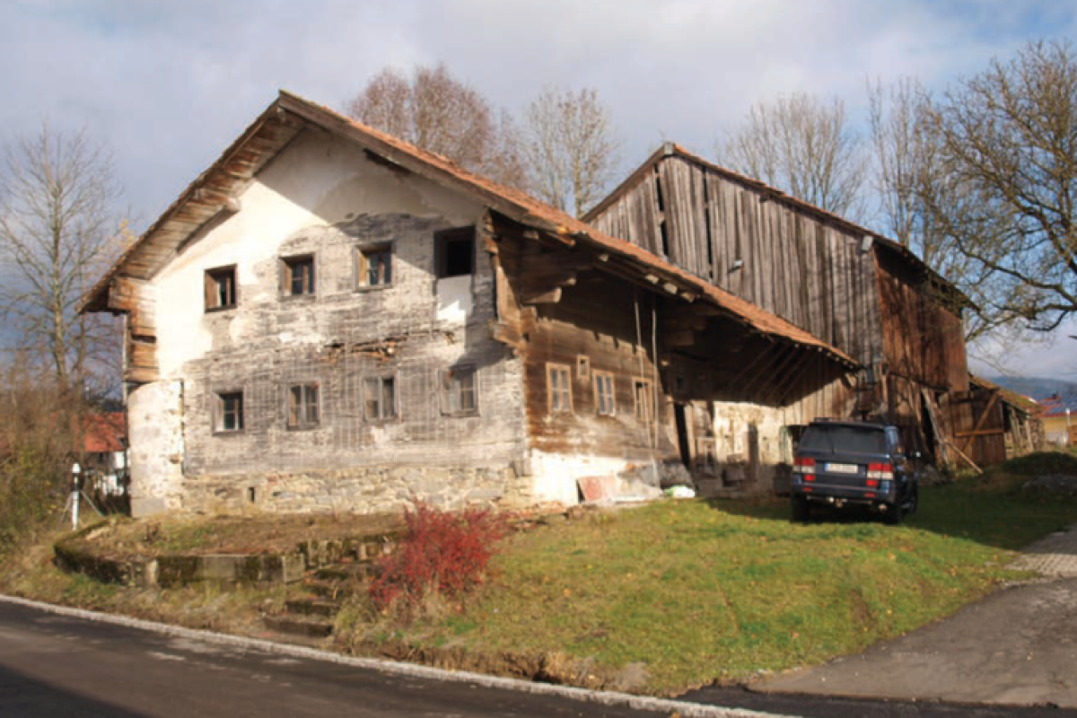 Ein niederbayerisches Waldlerhaus in seiner alten Form. Im Hintergrund ist eine marode Scheune ersichtlich.
