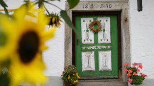 Grüne Haustür eines Bauernhauses. Im Vordergrund steht eine Sonnenblume