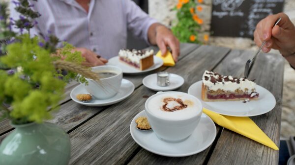 Auf einem Biergartentisch stehen zwei Kaffeetassen und zwei Kuchenteller mit Tortenstücken