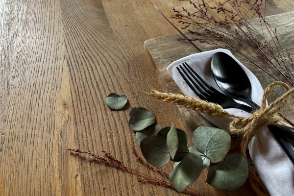 Ein Holztisch auf dem eine schön dekorierter Löffel und eine Gabel liegen.