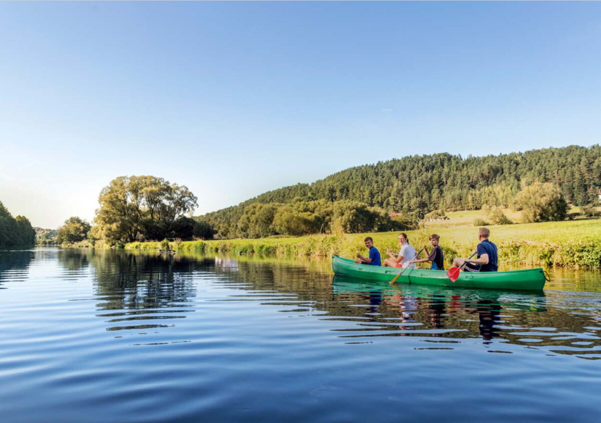 Ein Kanu mit vier Personen auf einem ruhigen Fluss.